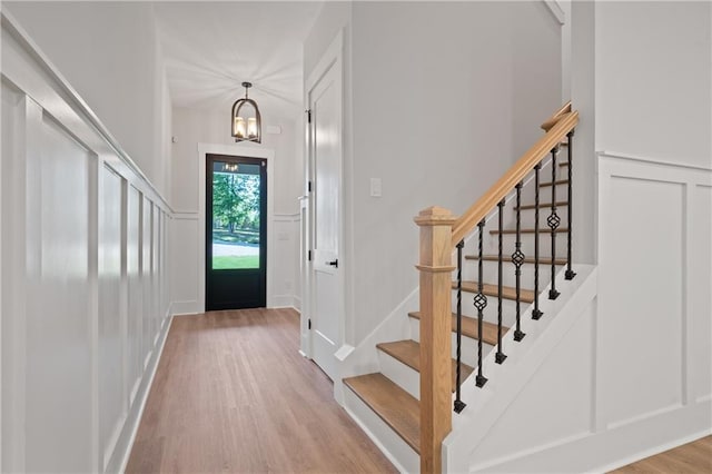 entryway with light wood finished floors, a chandelier, stairway, and a decorative wall