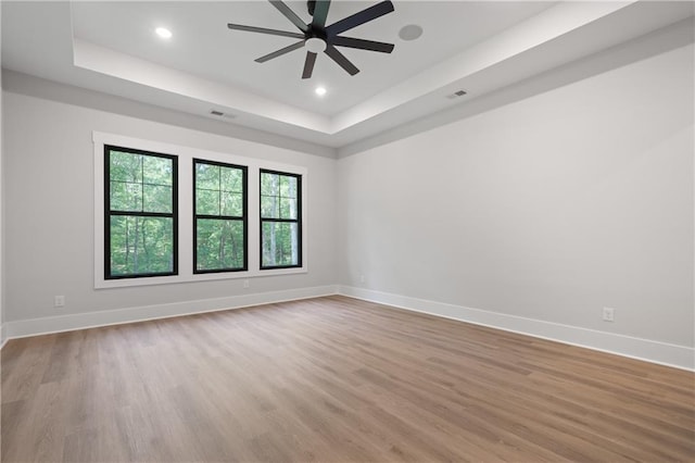 spare room featuring a tray ceiling, a ceiling fan, wood finished floors, baseboards, and recessed lighting