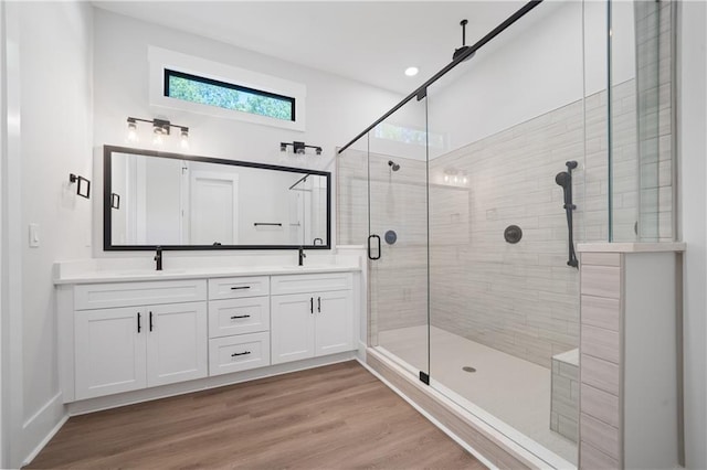 bathroom with a shower stall, double vanity, and wood finished floors