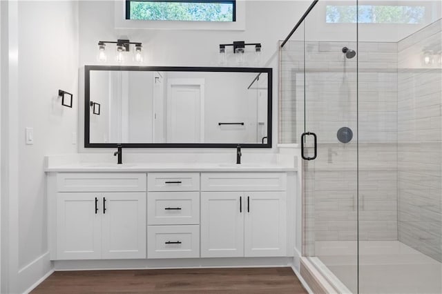 full bathroom with a stall shower, double vanity, wood finished floors, and baseboards