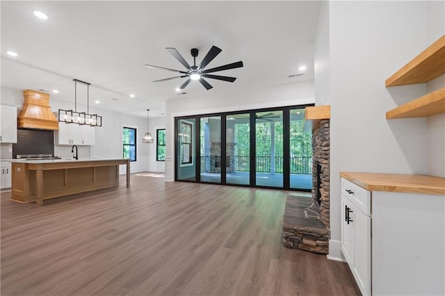 living room featuring wood finished floors, a ceiling fan, recessed lighting, a stone fireplace, and baseboards