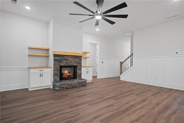 unfurnished living room with a decorative wall, stairs, ceiling fan, wood finished floors, and a stone fireplace