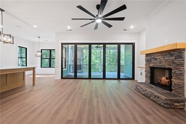 unfurnished living room with a stone fireplace, light wood-style flooring, a ceiling fan, plenty of natural light, and recessed lighting