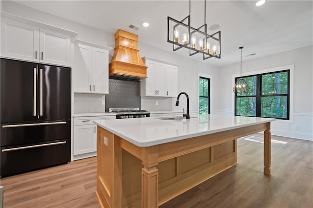 kitchen featuring high end black fridge, a sink, a chandelier, premium range hood, and recessed lighting