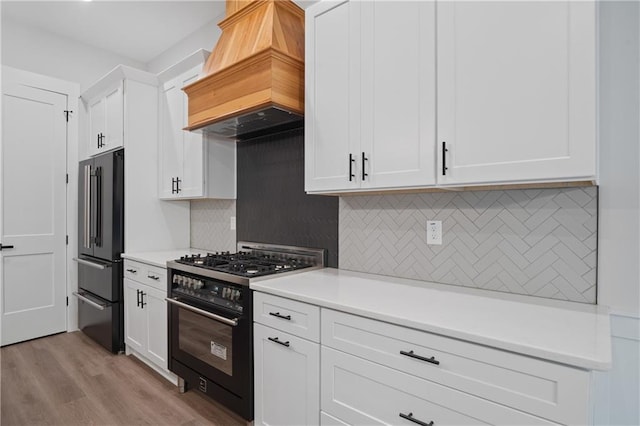 kitchen featuring premium appliances, premium range hood, light countertops, white cabinetry, and decorative backsplash