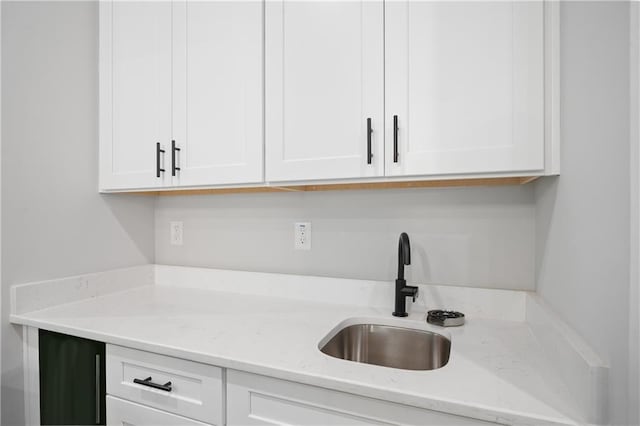 kitchen with a sink, white cabinetry, and light stone countertops