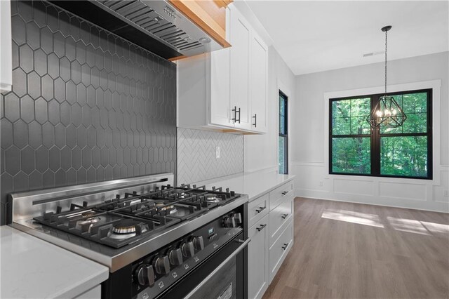 kitchen with range, wall chimney exhaust hood, light countertops, light wood finished floors, and a chandelier