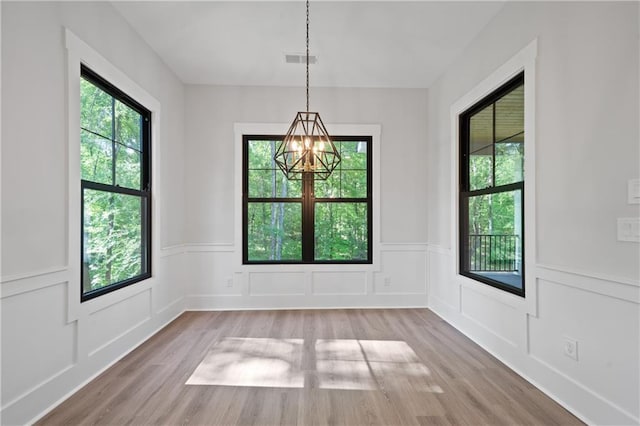 unfurnished dining area with a chandelier, wood finished floors, a decorative wall, and wainscoting