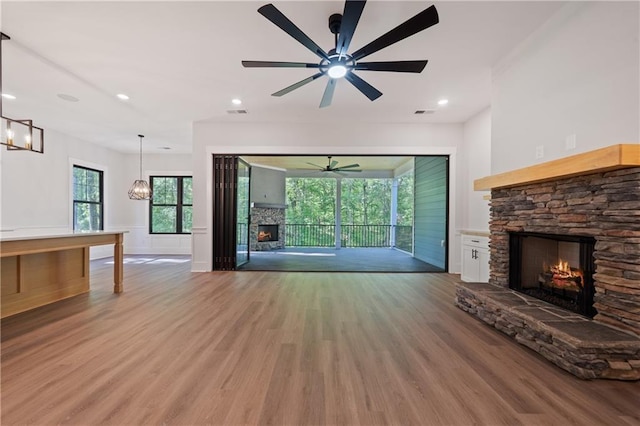 unfurnished living room featuring a stone fireplace, ceiling fan, light wood-type flooring, a wainscoted wall, and a chandelier