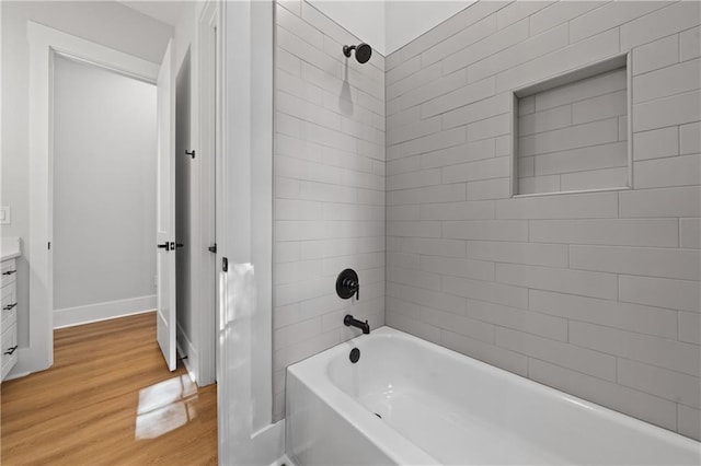 full bath featuring wood finished floors, washtub / shower combination, baseboards, and vanity