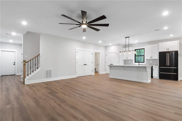 unfurnished living room featuring light wood-style floors, recessed lighting, a ceiling fan, stairs, and baseboards