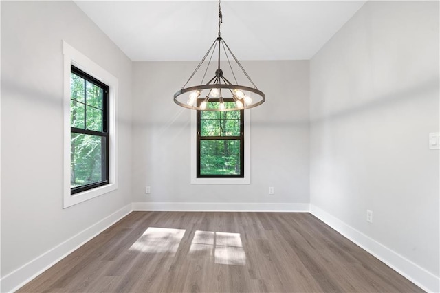 empty room featuring a chandelier, wood finished floors, and baseboards