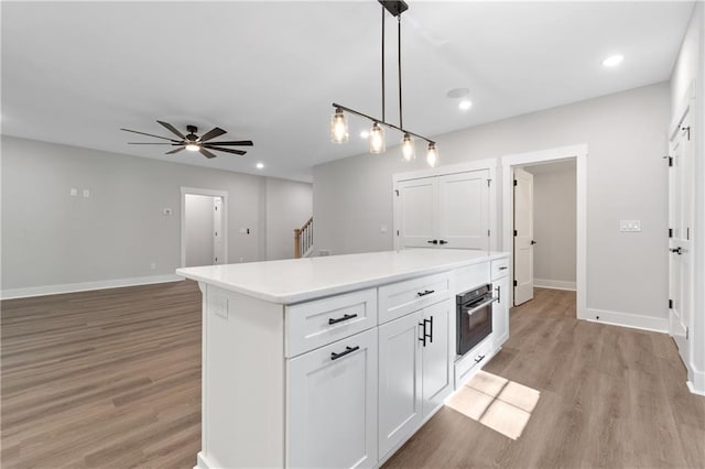 kitchen with oven, light wood finished floors, ceiling fan, baseboards, and white cabinets
