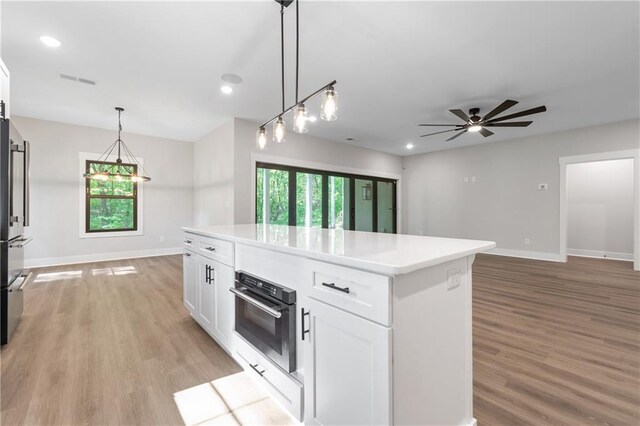 kitchen with oven, a kitchen island, white cabinetry, light wood-type flooring, and light countertops