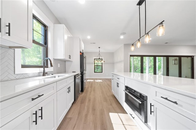 kitchen featuring stainless steel appliances, white cabinetry, decorative backsplash, light wood-type flooring, and pendant lighting