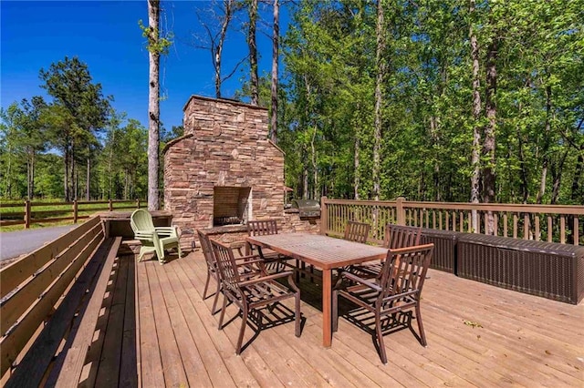 wooden terrace with an outdoor stone fireplace, area for grilling, and outdoor dining space