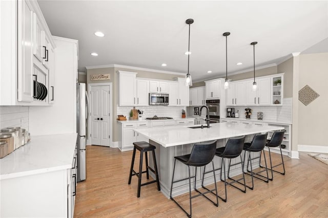 kitchen featuring appliances with stainless steel finishes, white cabinets, a sink, light wood-type flooring, and a kitchen bar