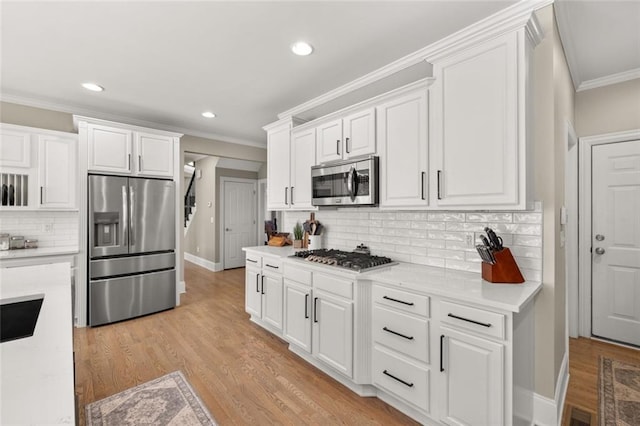 kitchen with light wood finished floors, appliances with stainless steel finishes, ornamental molding, light countertops, and white cabinetry