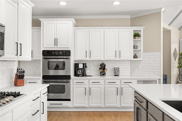 kitchen featuring white cabinets, light countertops, appliances with stainless steel finishes, light wood-type flooring, and crown molding