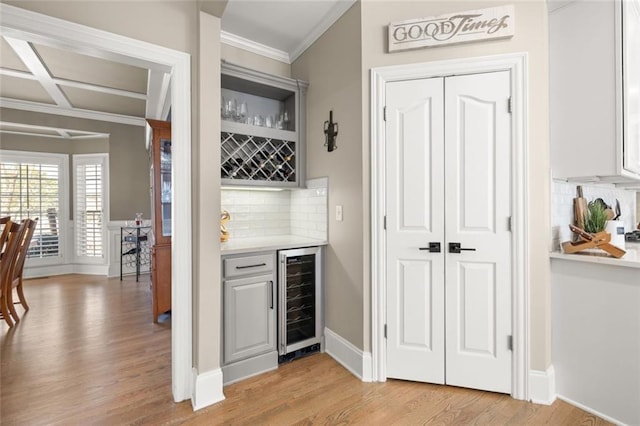 bar with light wood-style flooring, decorative backsplash, ornamental molding, a bar, and beverage cooler