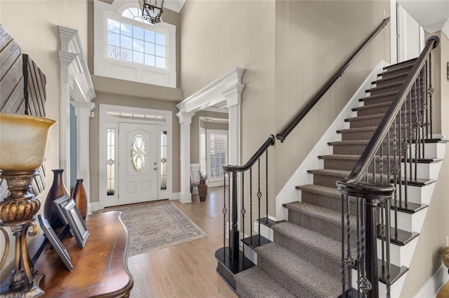 entryway with a towering ceiling, decorative columns, baseboards, and wood finished floors