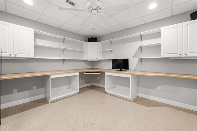 interior space with visible vents, baseboards, a drop ceiling, built in study area, and ceiling fan