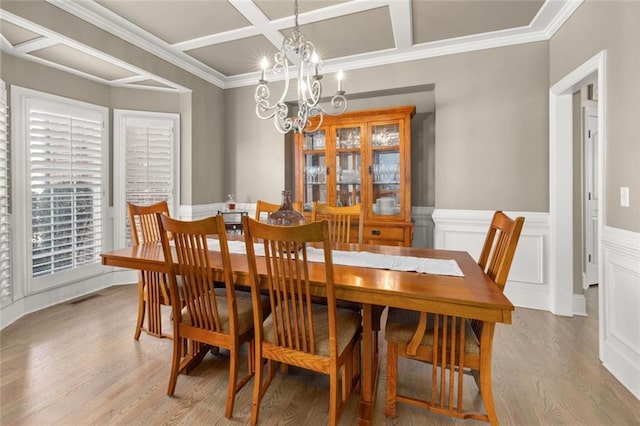 dining space featuring coffered ceiling, light wood-style floors, ornamental molding, wainscoting, and an inviting chandelier