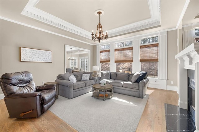 living room featuring a chandelier, a fireplace, wood finished floors, a tray ceiling, and crown molding