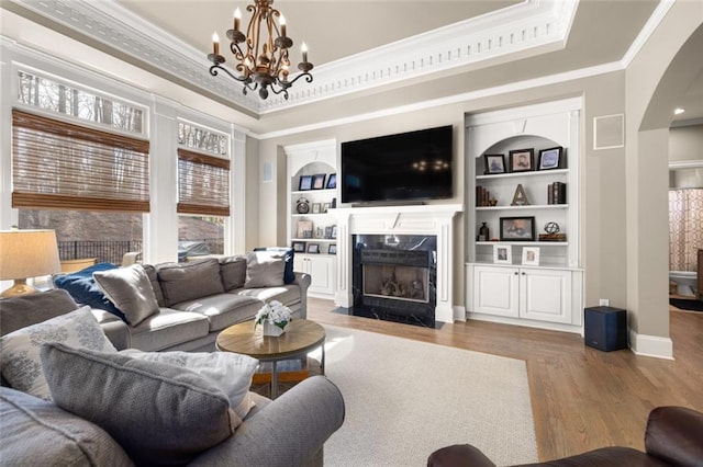 living room with arched walkways, built in shelves, a premium fireplace, and a raised ceiling