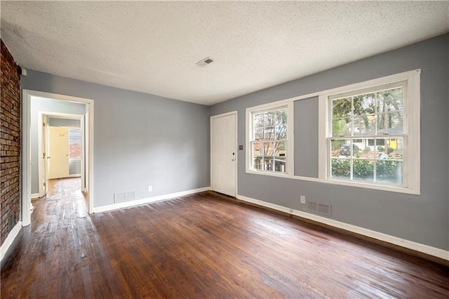 unfurnished room featuring a fireplace, a textured ceiling, dark wood-type flooring, and brick wall