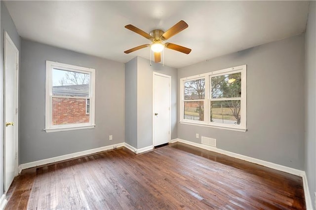 unfurnished bedroom with ceiling fan, a closet, dark wood-type flooring, and multiple windows