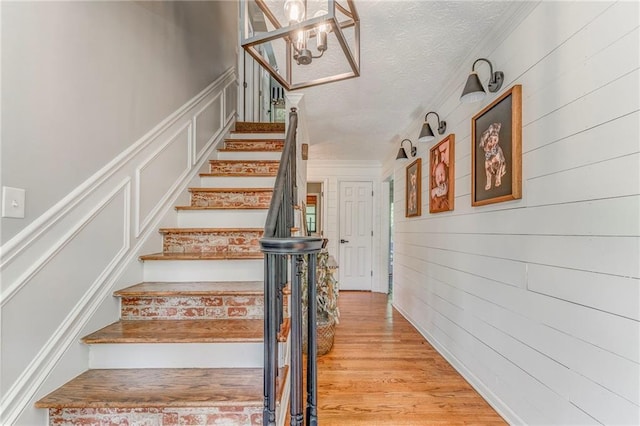323 Schoolhouse Rd, Rockmart, GA 30153 - stairs featuring a textured ceiling, a chandelier, a decorative wall, wood finished floors, and ornamental molding
