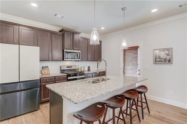 kitchen featuring stainless steel appliances, a sink, a kitchen breakfast bar, light wood finished floors, and dark brown cabinets