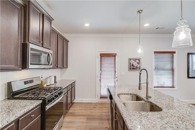 kitchen with appliances with stainless steel finishes, a sink, dark brown cabinets, light wood-style floors, and ornamental molding