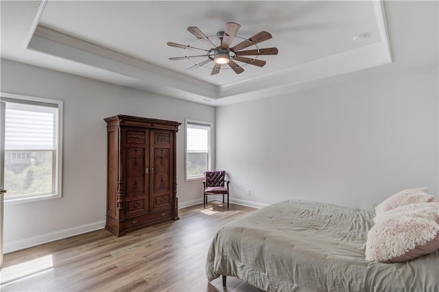bedroom featuring a tray ceiling, light wood-type flooring, baseboards, and ceiling fan