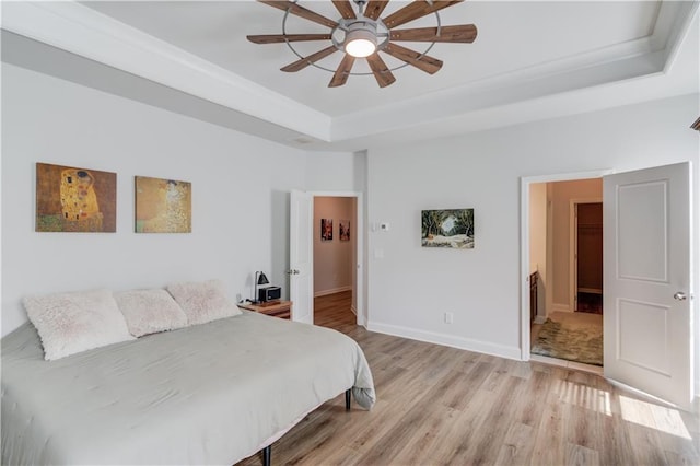 bedroom featuring a tray ceiling, light wood finished floors, baseboards, and ceiling fan