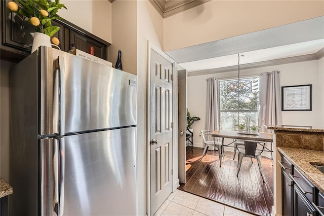 kitchen featuring decorative light fixtures, stainless steel fridge, ornamental molding, dark brown cabinetry, and light stone counters