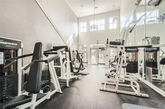 gym featuring an inviting chandelier, a healthy amount of sunlight, and a high ceiling