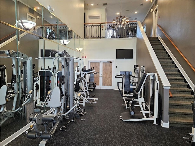 gym featuring a towering ceiling, french doors, and a chandelier