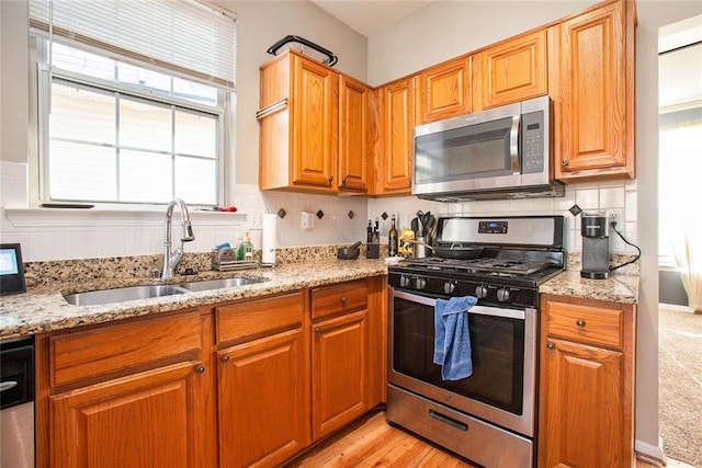 kitchen featuring sink, light hardwood / wood-style floors, backsplash, light stone countertops, and appliances with stainless steel finishes