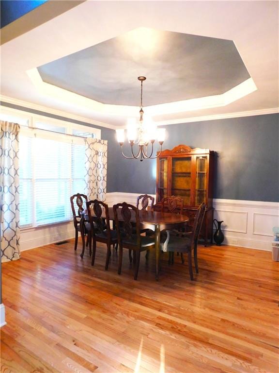 dining space with a chandelier, wood-type flooring, a tray ceiling, and ornamental molding