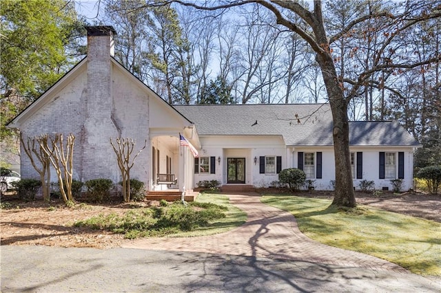 view of front of property featuring brick siding, a chimney, a front yard, and a shingled roof