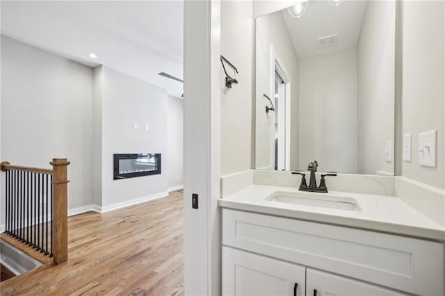 bathroom featuring wood finished floors, baseboards, vanity, and a glass covered fireplace