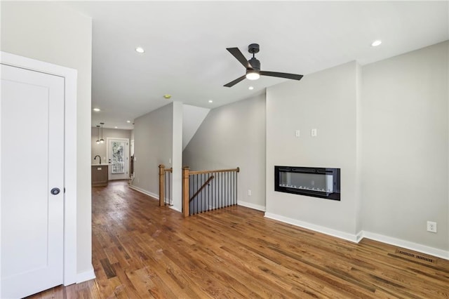 unfurnished living room featuring wood finished floors, a glass covered fireplace, recessed lighting, a ceiling fan, and baseboards