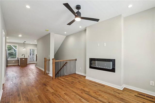 unfurnished living room with wood finished floors, a glass covered fireplace, recessed lighting, ceiling fan, and baseboards