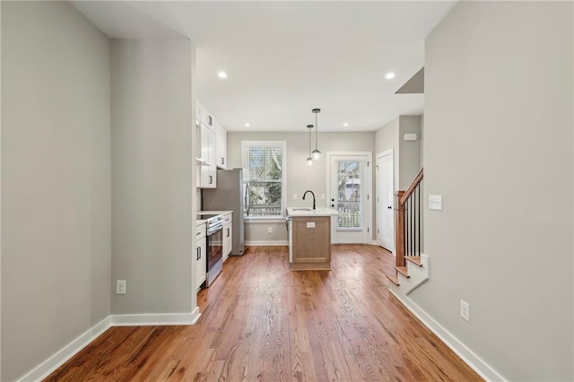 kitchen featuring stainless steel electric range oven, light countertops, an island with sink, baseboards, and light wood finished floors
