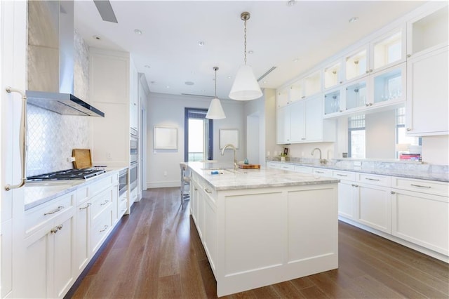 kitchen with a kitchen island with sink, decorative light fixtures, wall chimney exhaust hood, and white cabinets