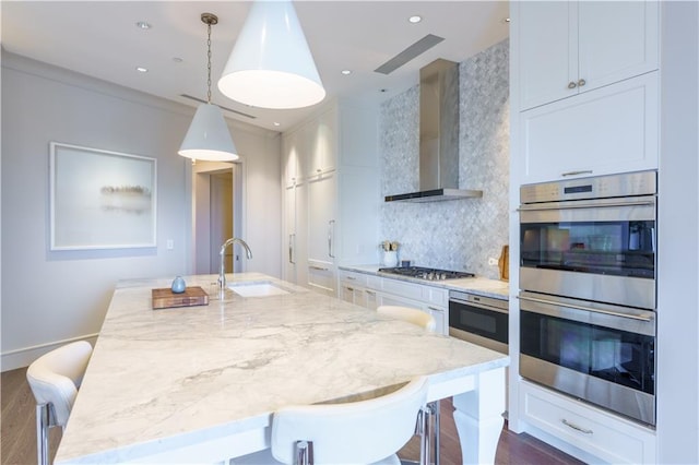 kitchen featuring wall chimney exhaust hood, stainless steel appliances, a breakfast bar area, and hanging light fixtures