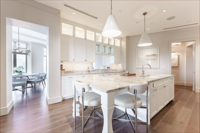 kitchen with pendant lighting, white cabinetry, an island with sink, sink, and light stone counters