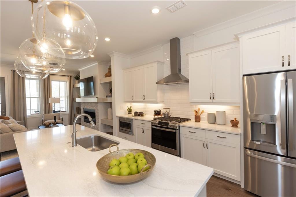 kitchen featuring wall chimney exhaust hood, sink, appliances with stainless steel finishes, an island with sink, and white cabinets